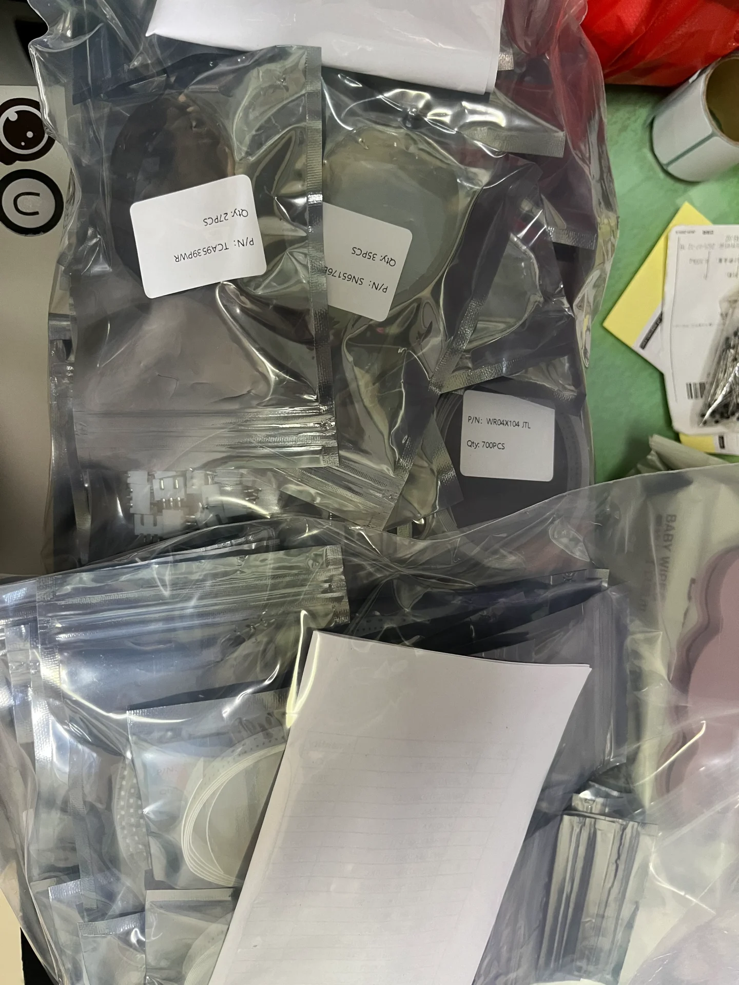 Multiple anti-static bags with labeled part numbers and quantities on a workbench, sorted for a BOM order