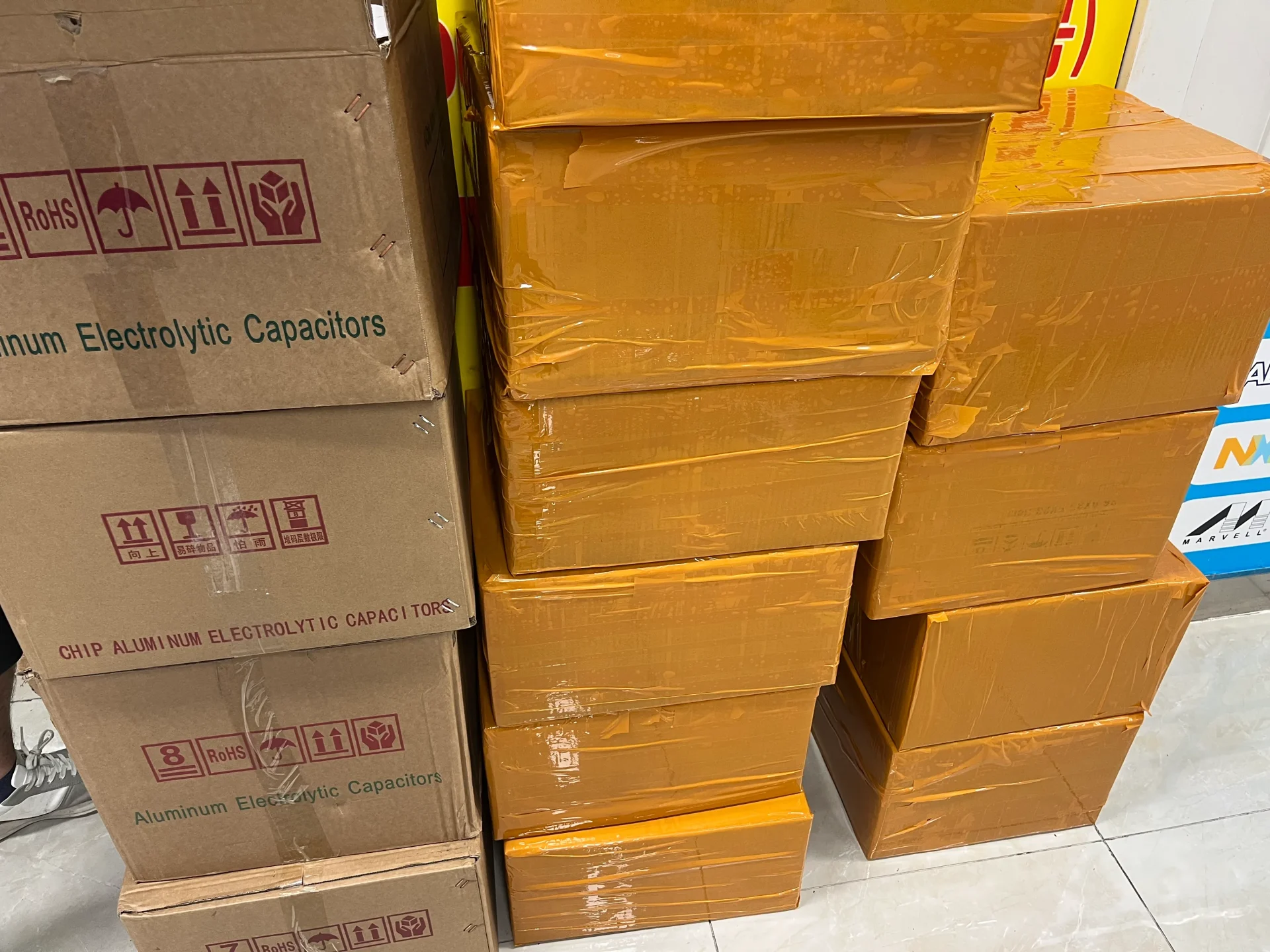 Aluminum electrolytic capacitor cartons alongside smaller orange shipping parcels, showing both bulk and split-order fulfillment